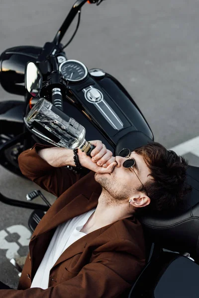 Elegante motociclista appoggiato testa sulla moto e bere alcol — Foto stock