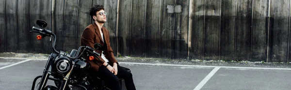 Panoramic shot of man in brown jacket resting on motorcycle — Stock Photo