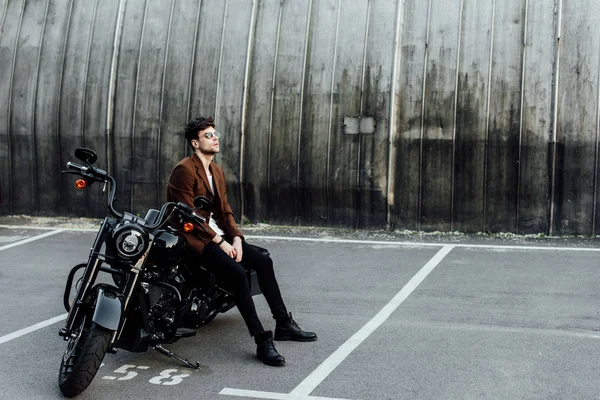 Full length view of handsome man in jacket resting on black motorcycle and looking away — Stock Photo