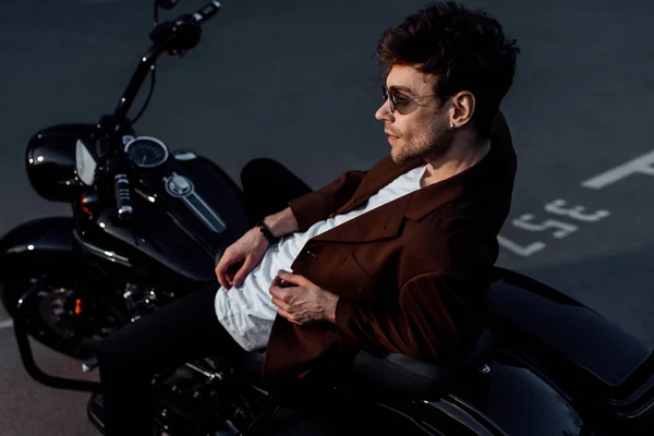 Jovem na jaqueta elegante encostado na motocicleta e olhando para longe — Fotografia de Stock