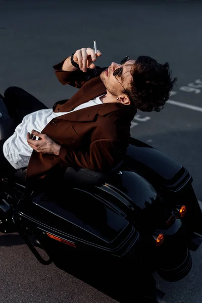 Молодой человек отдыхает на мотоцикле и курит сигарету — стоковое фото