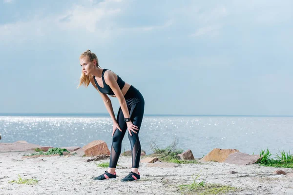 Attraente e stanca donna sportiva in piedi sulla spiaggia vicino al mare — Foto stock