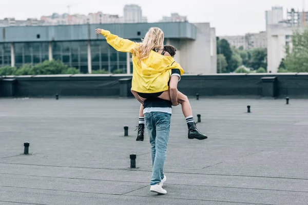 Back view of woman in yellow jacket playing with man on roof — Stock Photo