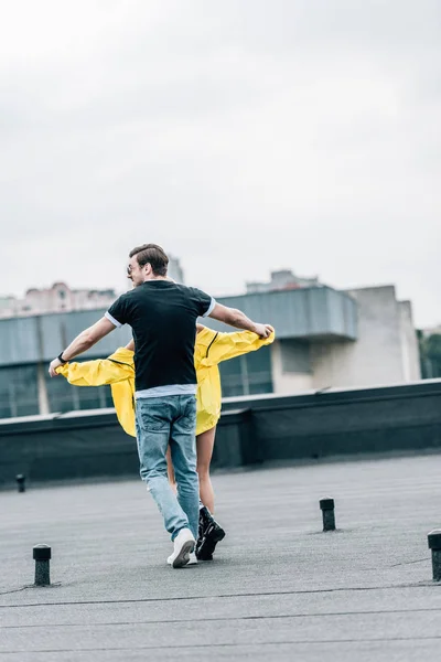 Vista trasera de la mujer en chaqueta amarilla y el hombre en jeans y camiseta de la mano - foto de stock