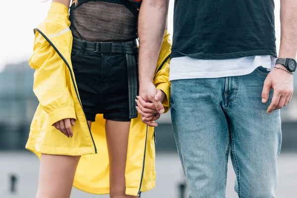 Обрезанный вид на женщину в желтой куртке и мужчину в джинсах, держащихся за руки — стоковое фото