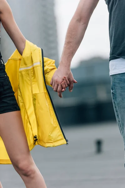 Обрезанный вид женщины в желтой куртке и мужчина, держащийся за руки — стоковое фото
