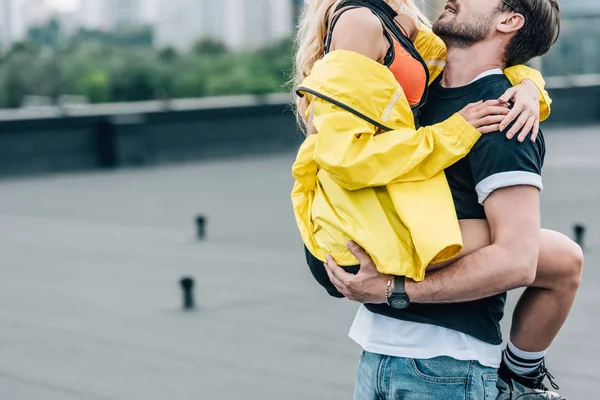 Vista recortada del hombre sosteniendo mujer en chaqueta amarilla en el techo - foto de stock