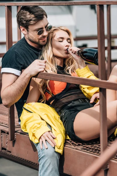 Bel homme dans des verres assis sur les escaliers et belle femme buvant du champagne — Photo de stock