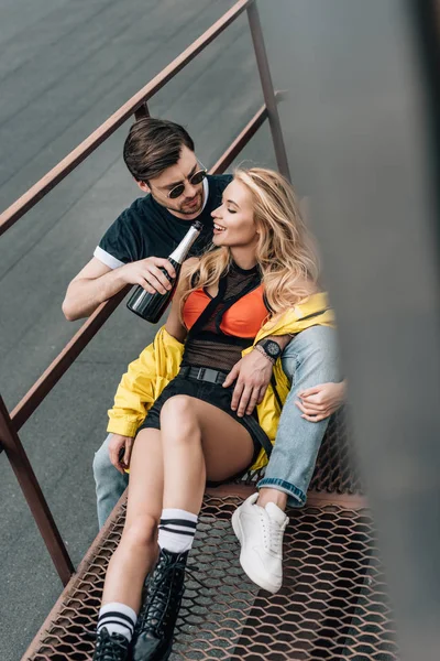 Hombre guapo en gafas sosteniendo botella y abrazando a mujer atractiva - foto de stock