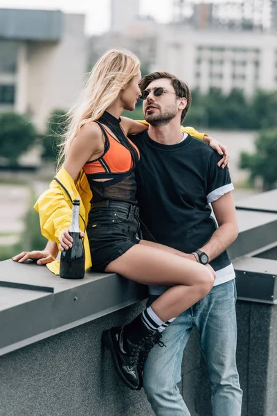 Mujer rubia con botella y hombre guapo en gafas abrazándose en el techo - foto de stock