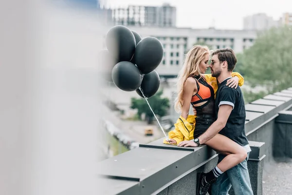 Selektiver Fokus der attraktiven Frau, die schwarze Luftballons in der Hand hält und sich mit dem Mann umarmt — Stockfoto