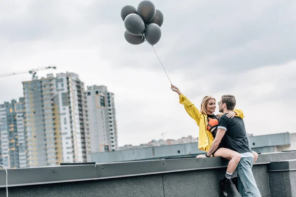 Attraktive Frau hält schwarze Luftballons und umarmt Mann — Stockfoto