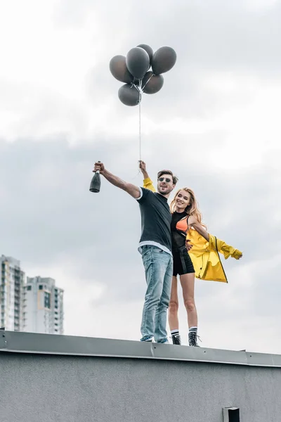 Attractive woman holding black balloons and handsome man holding bottle — Stock Photo