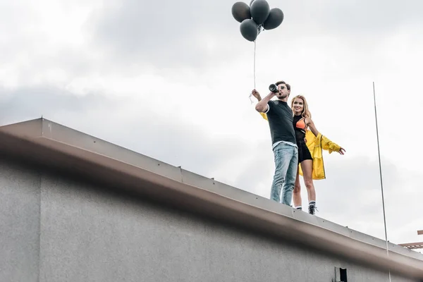 Attraktive Frau mit schwarzen Luftballons und schöner Mann, der Champagner trinkt — Stockfoto