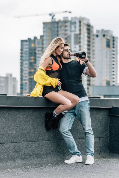 Mujer atractiva sentada en el techo y hombre guapo bebiendo champán - foto de stock