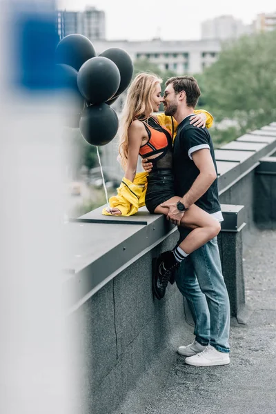 Mulher atraente segurando balões negros, beijando e abraçando com o homem — Fotografia de Stock