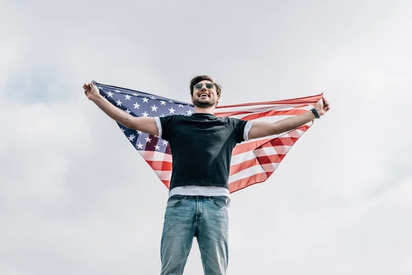 Homem bonito em óculos segurando bandeira americana e sorrindo no telhado — Fotografia de Stock