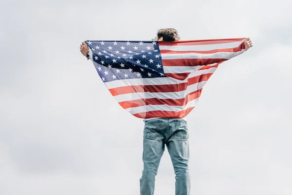 Back view of man in jeans holding american flag on roof — Stock Photo