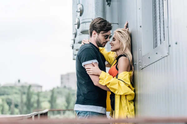 Handsome man in glasses and attractive woman kissing and hugging on roof — Stock Photo