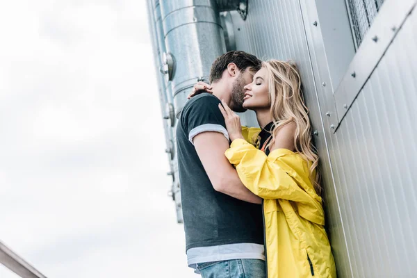 Hombre en camiseta y atractiva mujer besándose y abrazándose en el techo - foto de stock