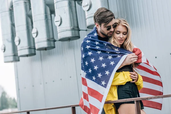 Attractive woman and handsome man with american flag hugging on roof — Stock Photo