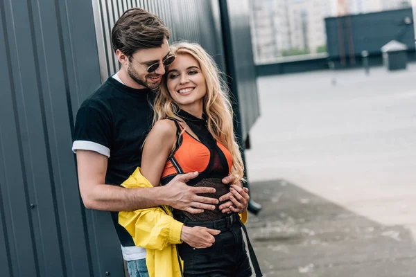 Attraktive Frau und schöner Mann mit Brille, die sich auf dem Dach umarmen und lächeln — Stockfoto