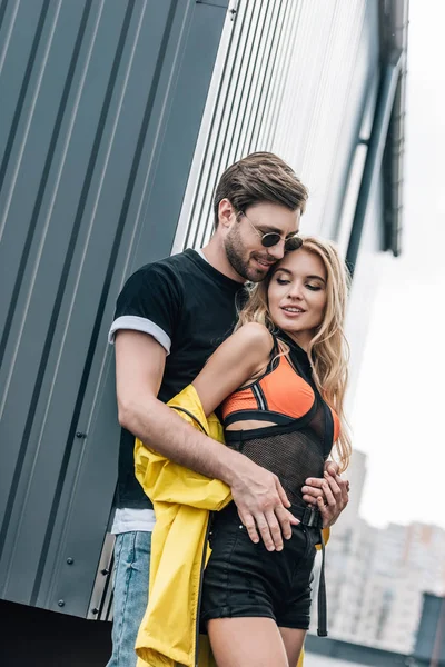 Séduisante femme et bel homme dans des lunettes étreignant sur le toit — Photo de stock