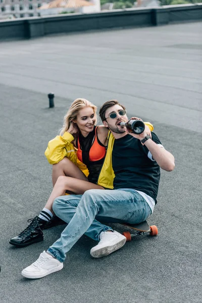 Mujer atractiva y hombre guapo en vasos sentados en el techo y beber champán - foto de stock