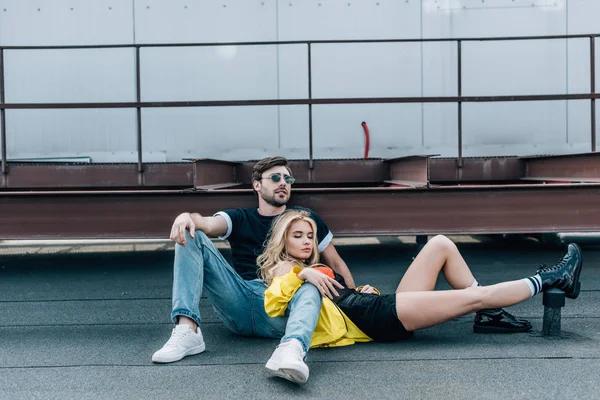 Atractiva mujer con los ojos cerrados y hombre guapo en gafas sentado en el techo - foto de stock