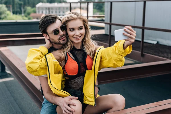 Hermosa mujer en chaqueta amarilla tomando selfie con hombre guapo - foto de stock