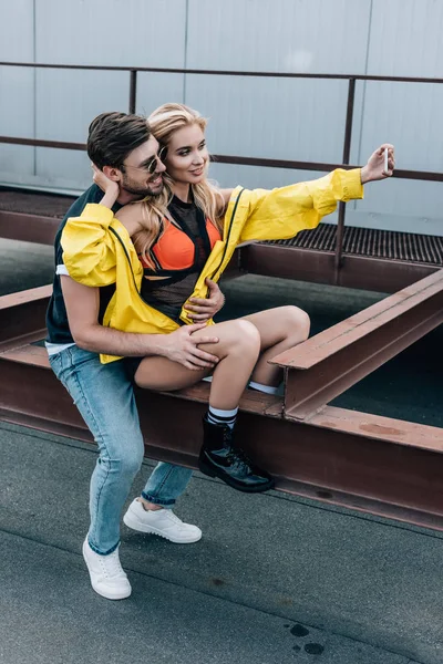 Atractiva y rubia mujer tomando selfie con hombre guapo - foto de stock