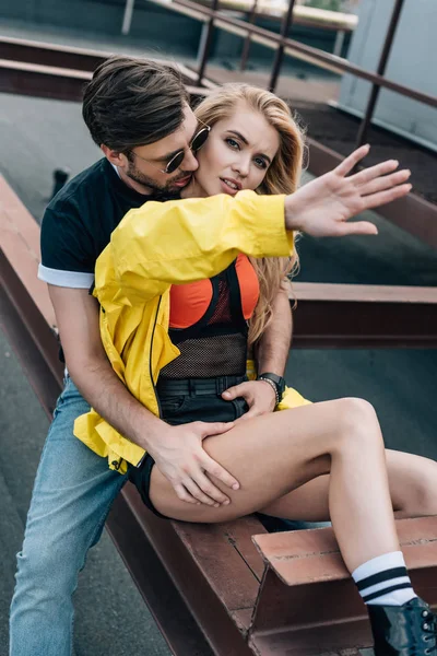 Attractive and blonde woman showing hand and handsome man hugging her — Stock Photo