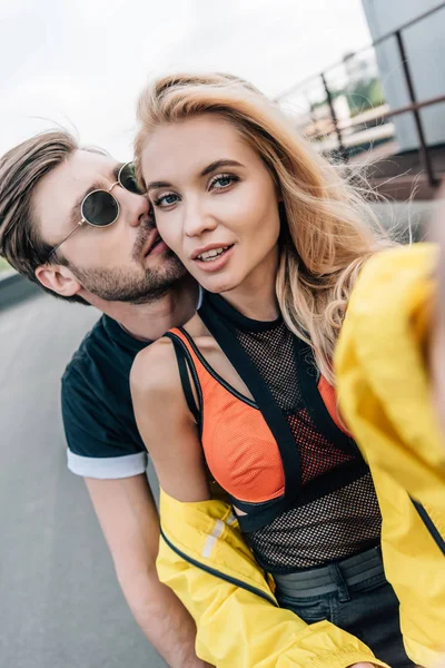 Atractiva y rubia mujer tomando selfie con hombre guapo - foto de stock
