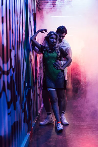 Attraktive und blonde Frau umarmt mit gutaussehendem Mann in der Nähe der Mauer — Stockfoto