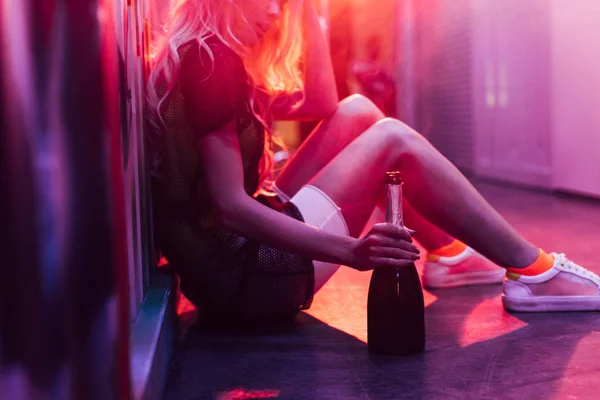 Vista ritagliata della donna seduta sul pavimento e bottiglia di tenuta — Foto stock