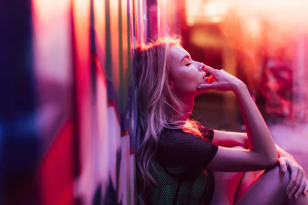 Side view of blonde woman with closed eyes sitting near wall — Stock Photo