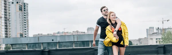 Panoramic shot of attractive and blonde woman and handsome man hugging on roof — Stock Photo
