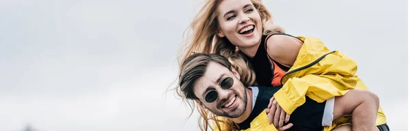 Panoramic shot of attractive and blonde woman and handsome man hugging and playing on roof — Stock Photo