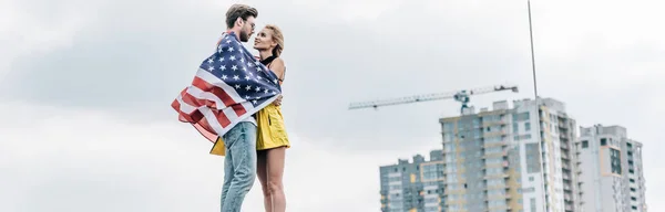 Plano panorámico de hombre con bandera americana abrazándose con mujer atractiva y rubia - foto de stock