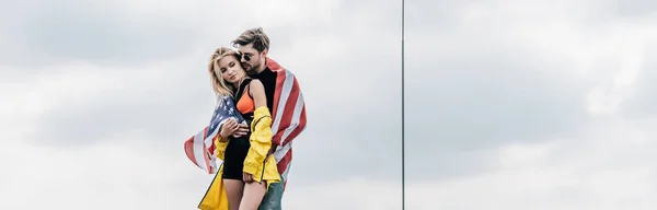 Colpo panoramico di uomo con bandiera americana che si abbraccia con donna attraente e bionda — Foto stock