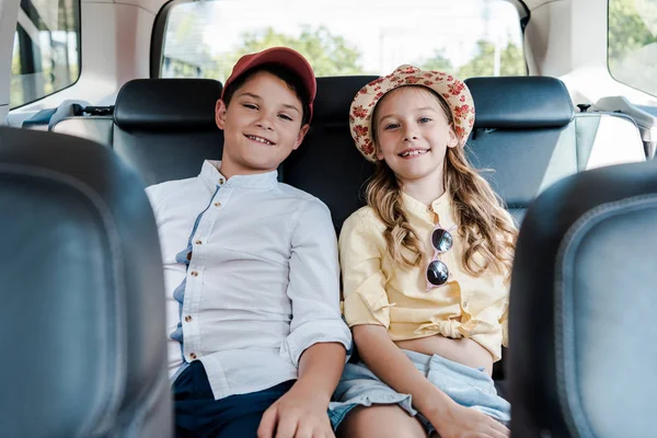 Enfoque selectivo de la hermana feliz y el hermano sonriendo mientras está sentado en el coche - foto de stock