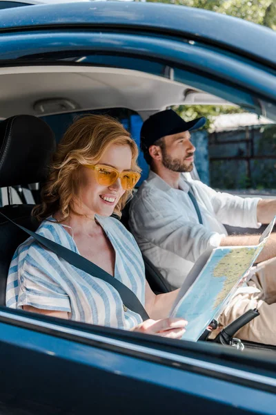 Selective focus of cheerful woman holding map while man driving car — Stock Photo