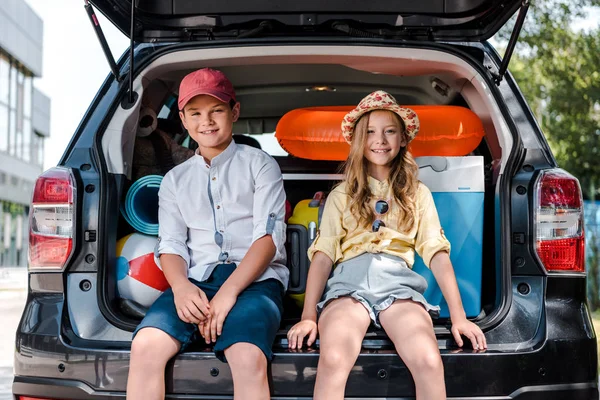 Щаслива сестра і брат сидять на багажнику і оглядаючись на камеру — стокове фото
