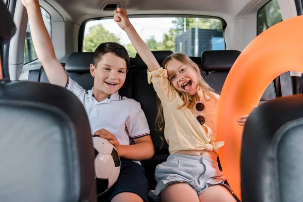 Selective focus of cheerful sister and brother celebrating and gesturing in car — Stock Photo