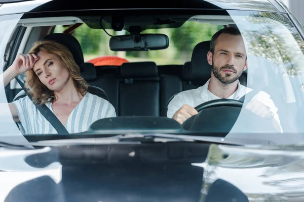 Selective focus of bearded man driving car near displeased woman — Stock Photo