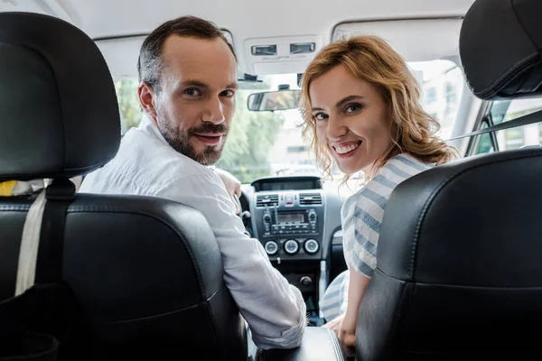 Selective focus of happy man and woman smiling while sitting in car — Stock Photo