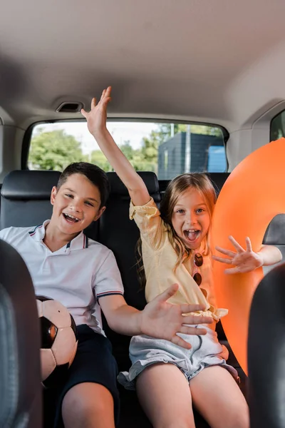 Messa a fuoco selettiva di sorella allegra e fratello gesticolando in auto — Foto stock