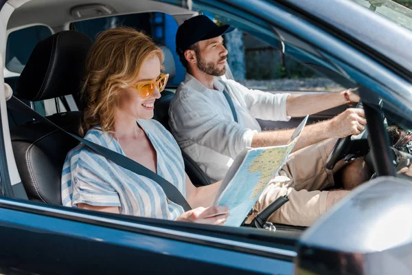 Foyer sélectif de la femme dans les lunettes de soleil en regardant la carte dans l'automobile près de l'homme — Photo de stock