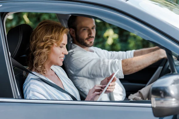 Foco seletivo da mulher feliz usando tablet digital no carro perto do homem — Fotografia de Stock