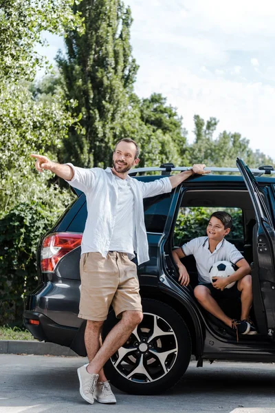 Счастливый человек стоит и показывает пальцем рядом с сыном в машине — стоковое фото